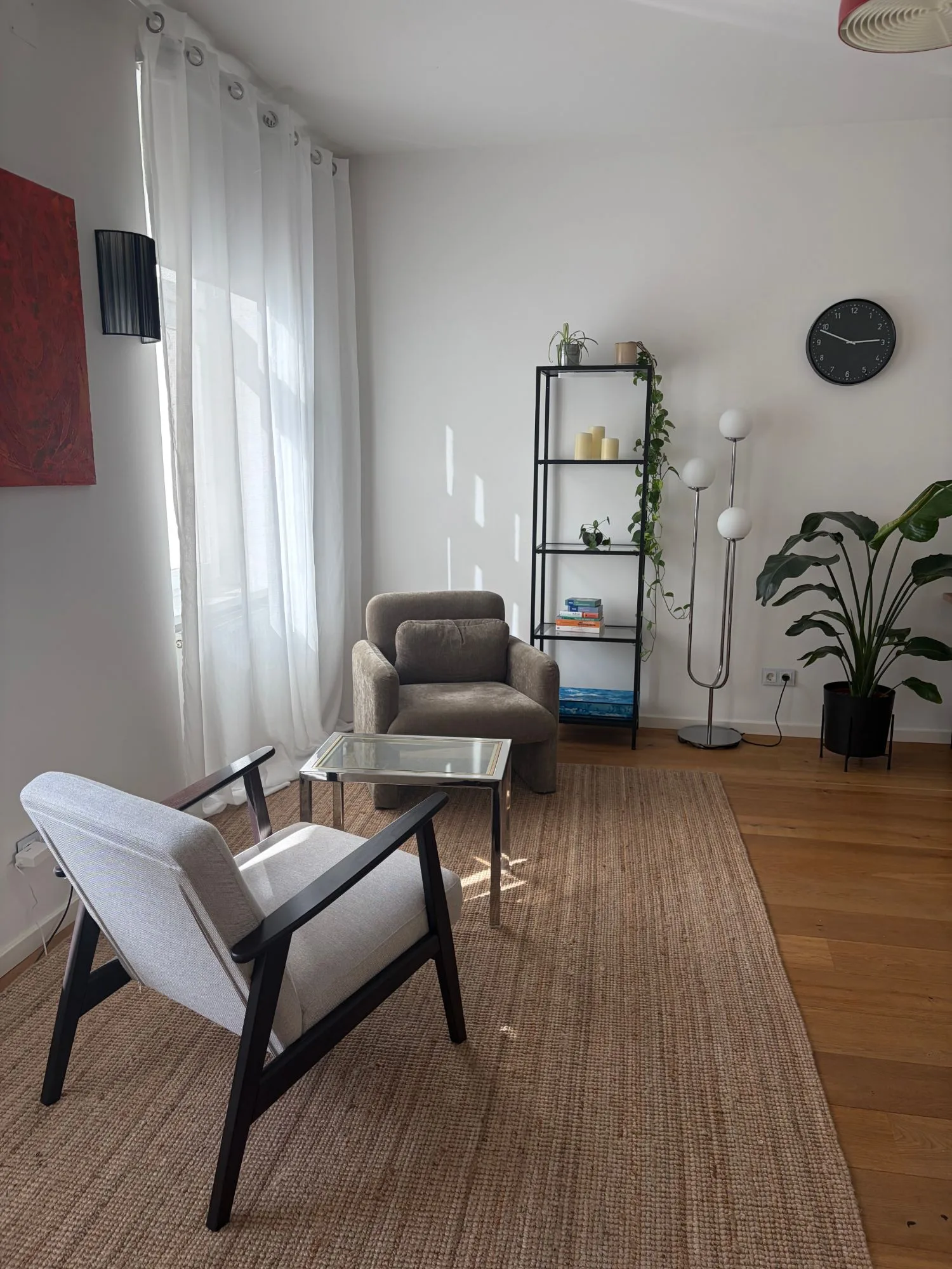 Praxisraum von Mona Fink in Wien: zwei Sessel an einem kleinen Glastisch, helles Fenster, Regal und Pflanzen